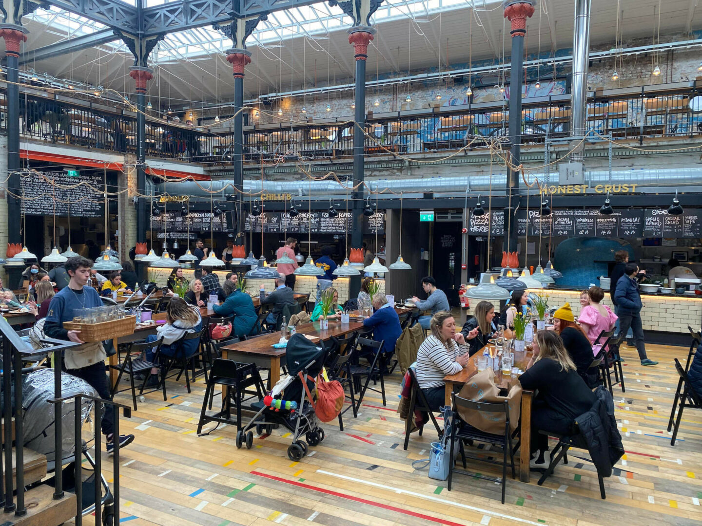 Interior of Mackie Mayor food hall in Manchester with people dining at long tables | Manchester Bites Food Tours